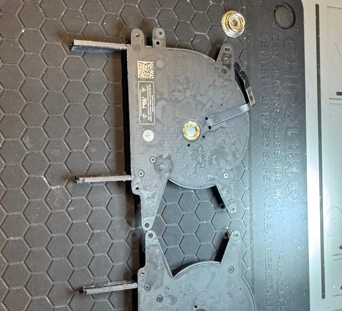 Los dos conjuntos de ventilador y bisagra de un portátil Apple, desmontados y colocados sobre el tapete de silicona antiestático