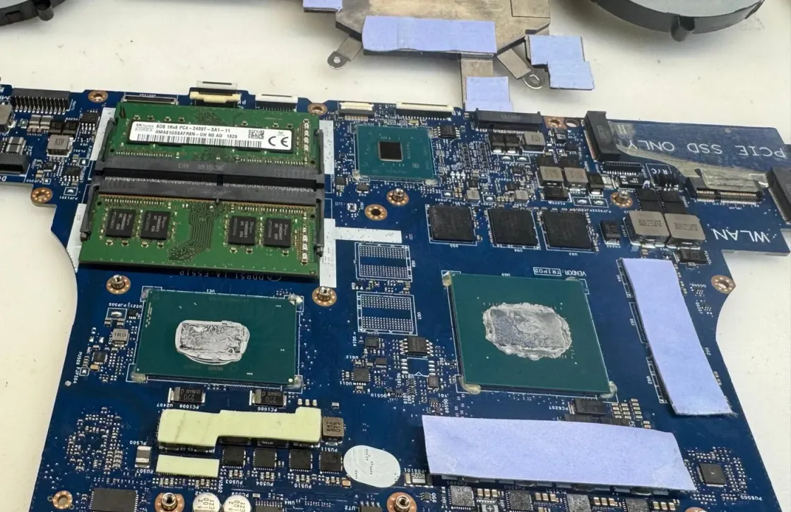 Placa de un portátil con el procesador y la gráfica al descubierto, con pasta térmica sobre los dos encapsulados y los zócalos de memoria al lado