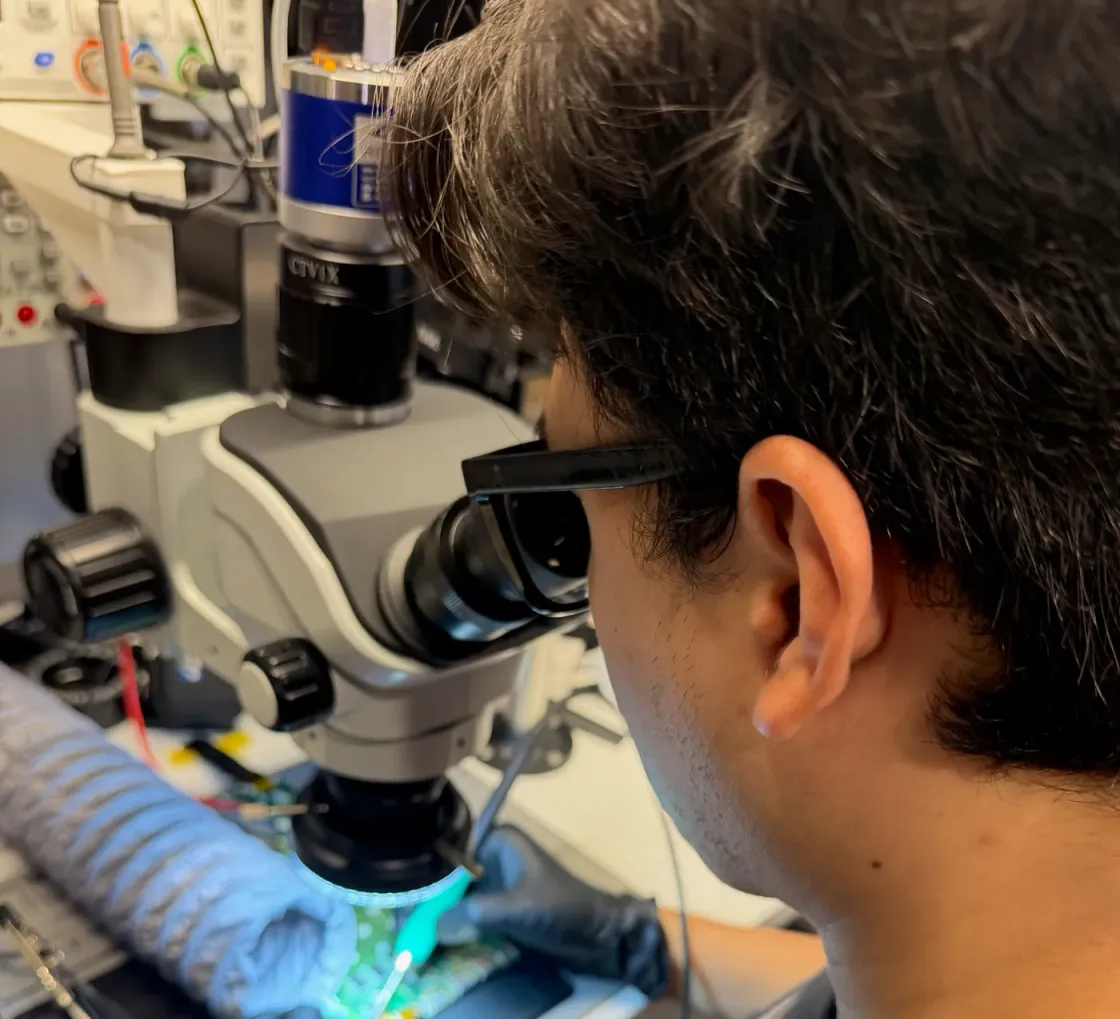 Técnico de BestFixing mirando por el microscopio estereoscópico una placa iluminada, visto por encima del hombro